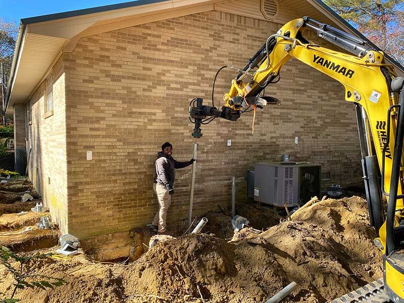 An excavator digging out the foundation around a brick home